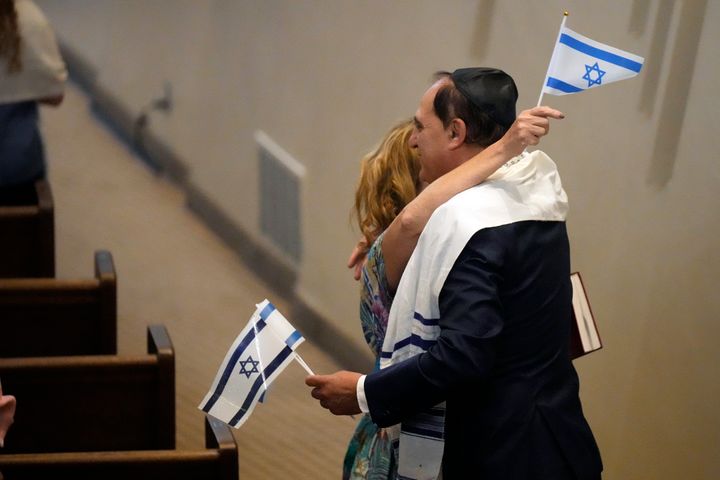 People hold Israeli flags as they hug during Shabbat Services at The Sinai Temple in Los Angeles, Saturday, Oct. 14, 2023. The temple's worshippers, the majority of whom have family in Israel, were on edge after recent pro-Palestinian rallies elsewhere in Los Angeles. The Shabbat service, themed "Sinai Temple Stands with Israel," featured prayers and songs for Israel, including the Israeli national anthem, to conclude the service as several people in the audience waved small Israeli flags. (AP Photo/Damian Dovarganes)